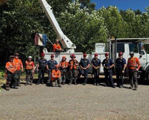 A group of men, some in orange vests, stand in front of a bucket truck.