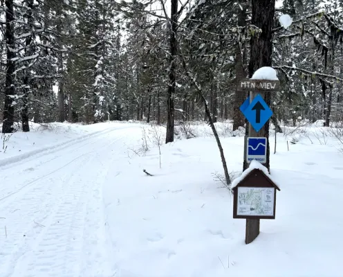 A snowy trail with a sign post marking the way forward